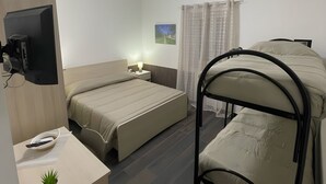 Habitació d'hotel amb un llit, un escriptori amb una planta, una televisió i una finestra amb cortines.