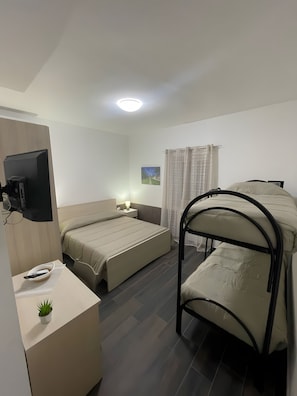 Habitació d'hotel amb llit, escriptori, televisió, finestra amb cortines i radiador.