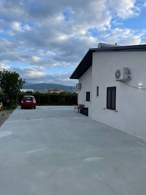 Un edifici amb un aparell d'aire condicionat, una banca i un cotxe vermell estacionat al davant.