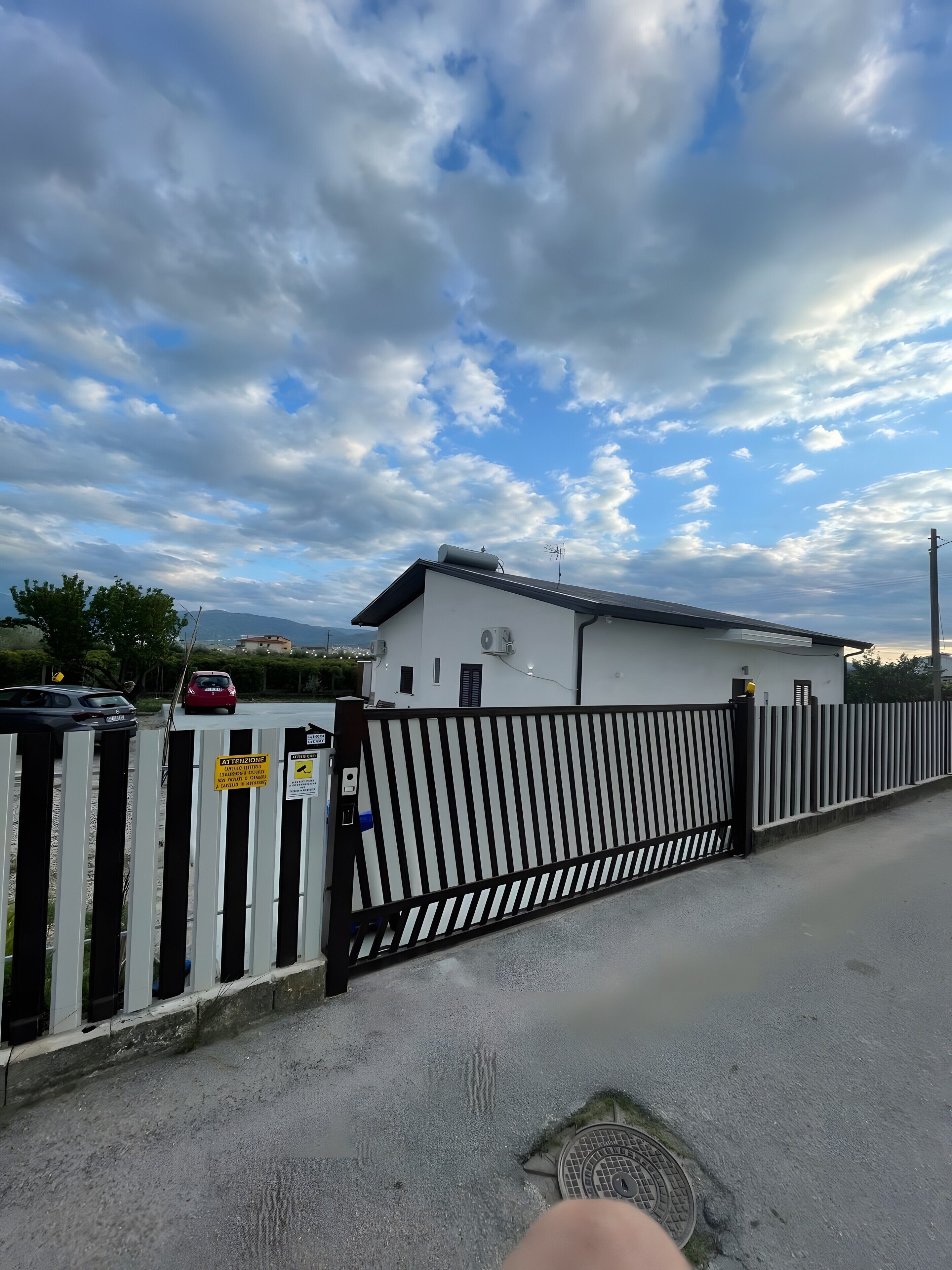 A gated parking area with a white building, a metal fence, and a clear sky.