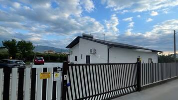 A gated parking area with a white building, a metal fence, and a clear sky.