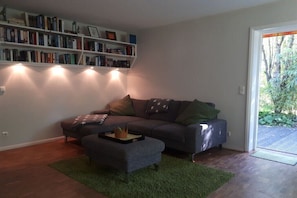 Ein Wohnzimmer mit einer Couch, einem Hocker und einem Bücherregal voller Bücher.