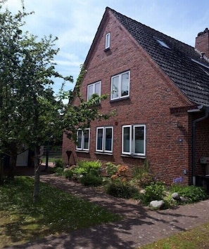 Ein rotes Backhaus mit geneigtem Dach, zahlreichen Fenstern und einem Garten mit Pflanzen und einem Baum.