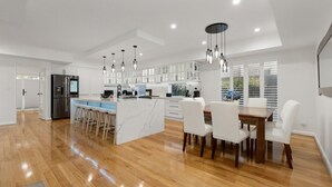 A modern kitchen with white cabinets, a central island, and bar stools. - Harbour Rise Luxury Family Retreat (Hillarys)