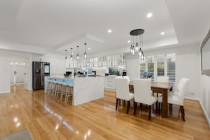A modern kitchen with white cabinets, a central island, and bar stools. - Harbour Rise Luxury Family Retreat (Hillarys)