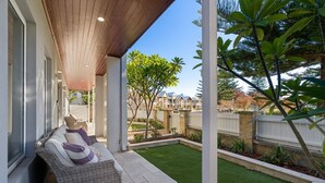 A covered patio with a wicker sofa, a small garden, and a view of neighboring houses. - Harbour Rise Luxury Family Retreat (Hillarys)