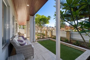 A covered patio with a wicker sofa, a small garden, and a view of neighboring houses. - Harbour Rise Luxury Family Retreat (Hillarys)