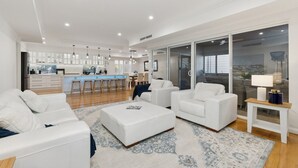 A modern living room with white furniture, a kitchen in the background, and a large sliding glass door to the right. - Harbour Rise Luxury Family Retreat (Hillarys)