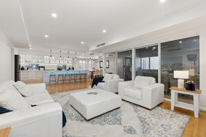 A modern living room with white furniture, a kitchen in the background, and a large sliding glass door to the right. - Harbour Rise Luxury Family Retreat (Hillarys)