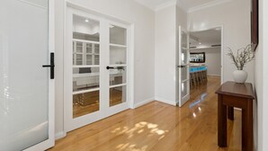 A hallway with a wooden floor, white walls, and a kitchen area visible through an open door. - Harbour Rise Luxury Family Retreat (Hillarys)