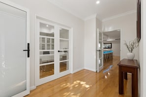 A hallway with a wooden floor, white walls, and a kitchen area visible through an open door. - Harbour Rise Luxury Family Retreat (Hillarys)