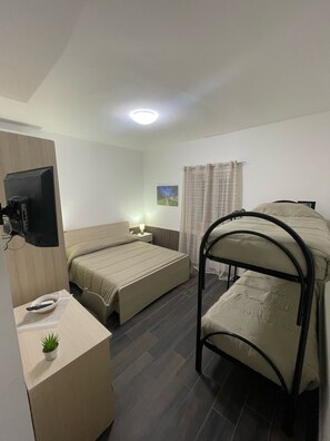 Une petite chambre moderne, équipée d’un lit, d’un bureau avec un ordinateur, d’une télévision et d’une fenêtre avec des rideaux.