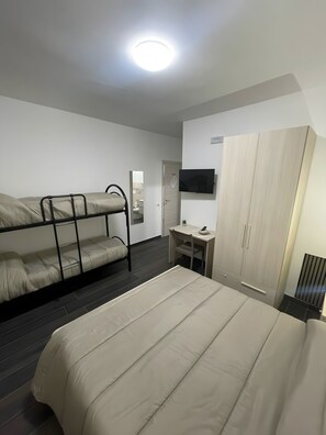Een kamer met stapelbedden, een bureau, een televisie en een kledingkast.