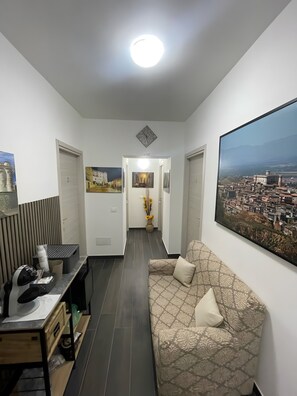 Een moderne woonkamer met een bank, een bureau met een printer, een groot stadsgezicht in een lijst en een gang naar een andere kamer.