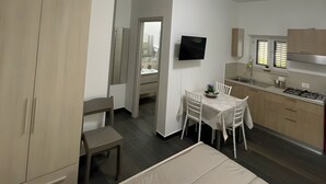 Une chambre avec un lit, une petite table avec des chaises, une télévision et une kitchenette équipée d’une cuisinière.