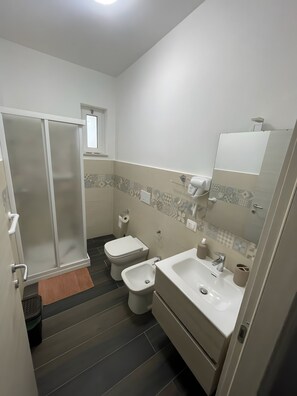 Et lille badeværelse med brusebad, toilet, bidet og håndvask.