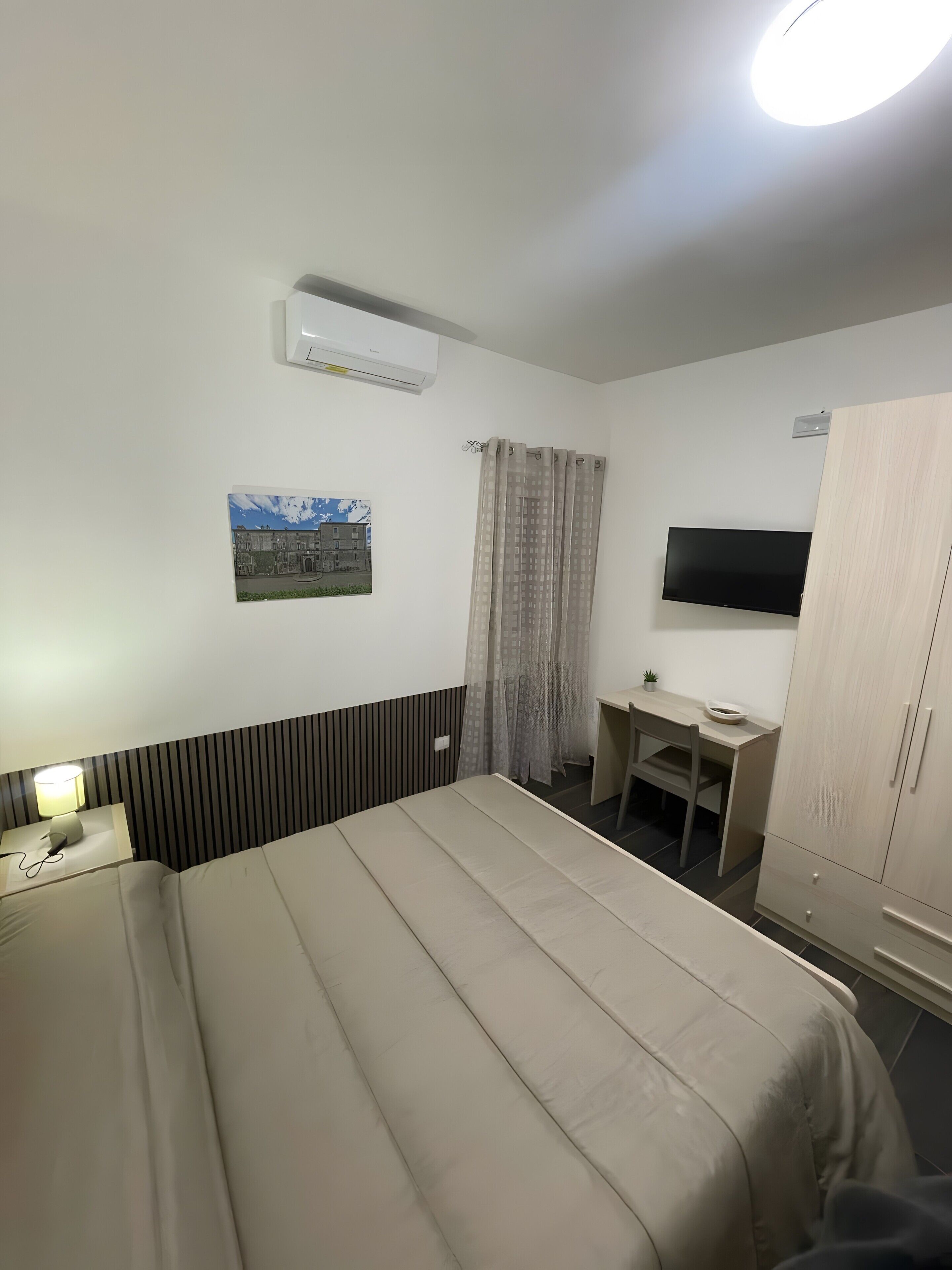 Une chambre d’hôtel avec un lit, un bureau, une télévision et une fenêtre avec des rideaux.