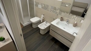 Une salle de bain moderne équipée d’une douche, de toilettes, d’un bidet et d’un lavabo avec un miroir au-dessus.
