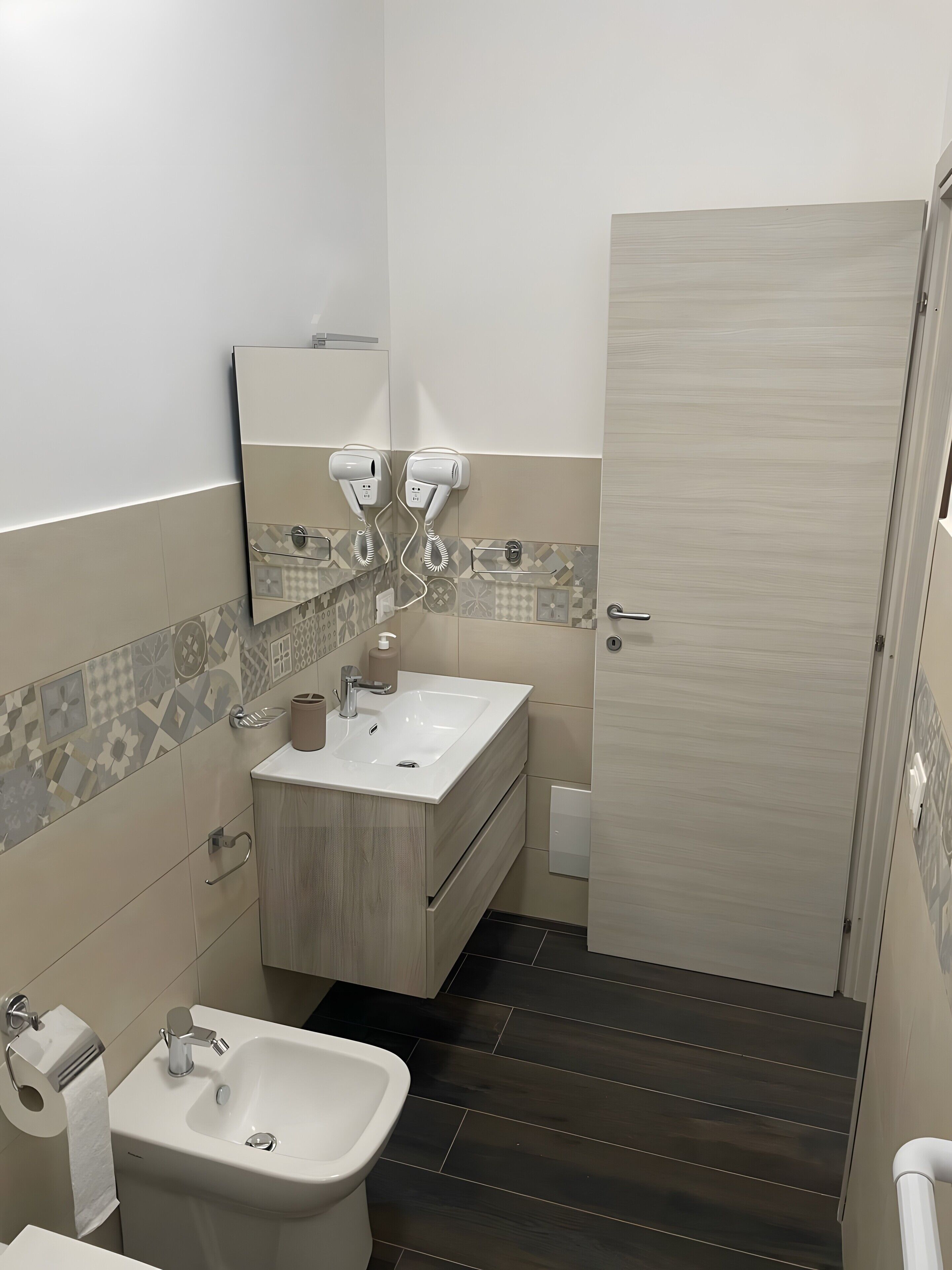 A bathroom with a sink, mirror, hairdryer, and dark wooden flooring.