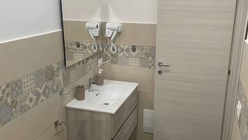 A bathroom with a sink, mirror, hairdryer, and dark wooden flooring.