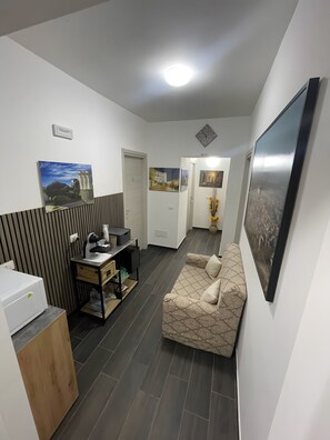 En moderne stue med sofa, sofabord, printer og skrivebord med computer. Væggene er pyntet med billeder, og der er en dør til et andet rum.