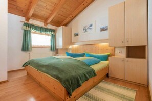 Ein Schlafzimmer mit einem hölzernen Bett, einem Fenster mit Vorhängen, einem Kopfteil und einem an der Wand befestigten Schrank.