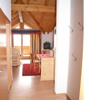 Ein Zimmer mit Holzbalkendecke, einer Essecke mit Tisch und Stühlen, einem Fernseher und einem roten Teppich.