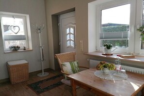 A room with a wooden table, wicker chair, and a window with a view. - Holiday home with 1 bedroom (Plau am See)