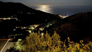 A night view of a coastal town with a prominent moon, hills, and distant city lights. - B&B Bella Vita (Moneglia)
