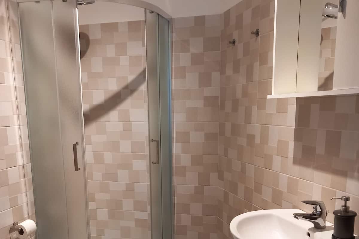 Ett badrum med en dusch som är avskärmad med glasväggar, en toalett, ett handfat och en spegel.