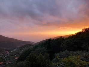 Paisaje montañoso con atardecer, líneas eléctricas y edificios dispersos.