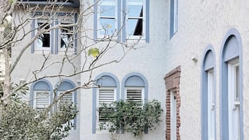 Una casa de dos pisos con fachada de ladrillo, varias ventanas y un pequeño jardín con plantas en macetas.