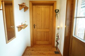 Eine Holztür mit einem kleinen Regal darüber, ein Kranz an der Wand und ein Fenster zur Rechten.
