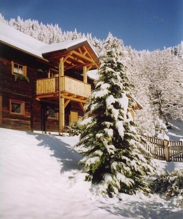 Eine Blockhütte mit Balkon, umgeben von schneebedeckten Bäumen.
