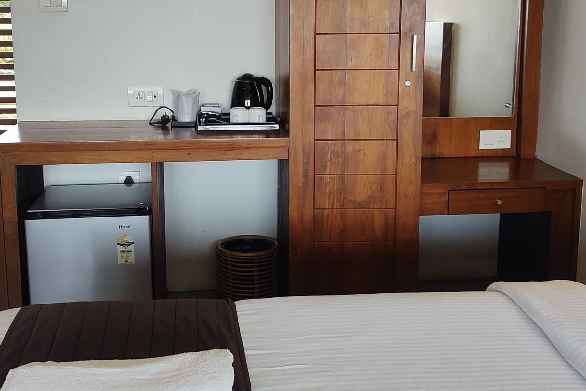 Habitación de hotel con cama, escritorio con espejo, cafetera y un pequeño calentador.