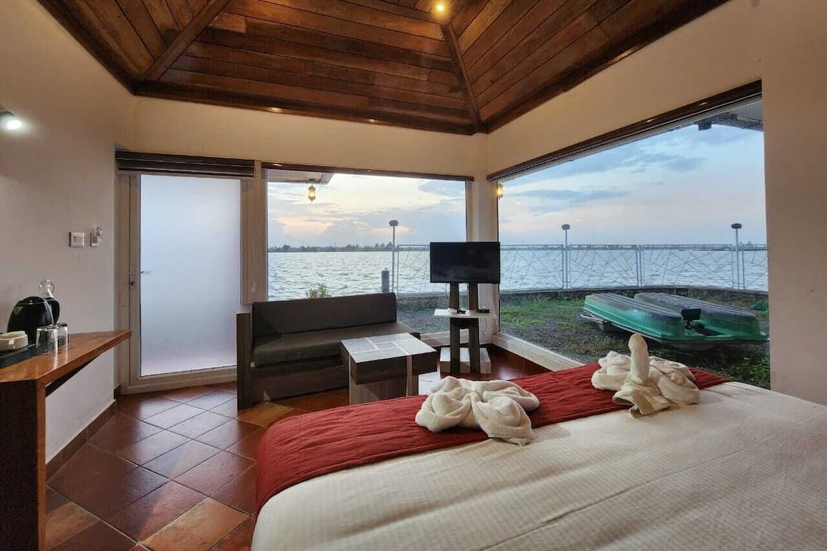 Un dormitorio con una cama grande, televisor, sofá y vista al agua.