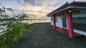 Un pequeño edificio de paredes blancas y techo rojo, ubicado cerca de una masa de agua con una valla al fondo.