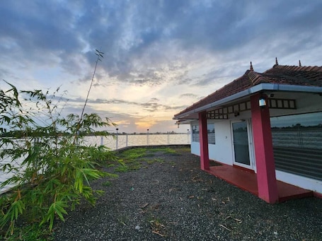 A small building with a red roof and white walls, situated near a body of water with a fence in the background.. MIRAS PMC Lakeshore Resort