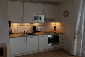 A compact kitchen with a microwave, stove, sink, and cabinets. - No. 2 in the Norderoog house (Borkum)