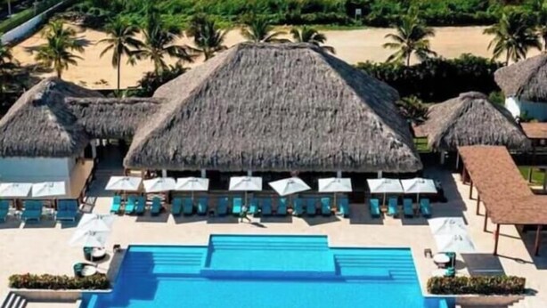 Un área de piscina en un resort con sombrillas de paja, sillas de descanso y una piscina azul cristalina.
