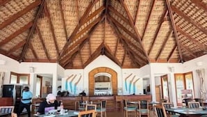 Un comedor espacioso con mesas y sillas de madera, un alto techo de madera y un arco central.