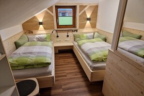 Ein kleiner, hell eingerichteter Raum mit zwei Holzbettställen, einem Tisch und einem Fenster mit Blick nach draußen.