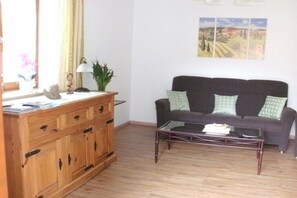 Ein Wohnzimmer mit einer Couch, einem Couchtisch, einem Holzschrank und einem Fenster mit Vorhängen.