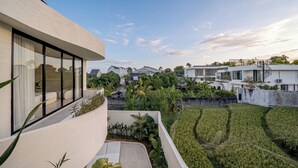 A modern building with large windows, a balcony, and a view of a residential area with houses and a garden. - IVY Villa 2 (Pererenan)