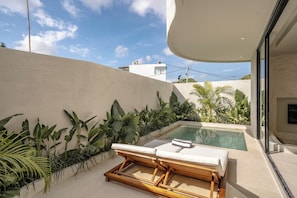 Un área de piscina moderna con dos sillas de descanso, una piscina pequeña y exuberante vegetación tropical.