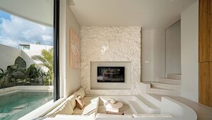 A modern interior with a stone wall, a TV mounted above a fireplace, a pool visible through a large window, and a curved seating area. - IVY Villa 2 (Pererenan)