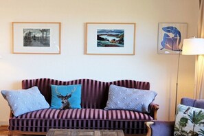 A striped sofa with decorative pillows, a framed landscape painting, and a lamp. - House with lake view (Ratzeburg)