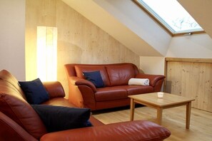 A loft-style room with a sloped ceiling, a brown leather sofa, a wooden coffee table, and a large window providing natural light. - Holiday apartment with 2 bedrooms (Eigeltingen)
