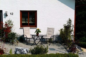 A white building with the number 12, a window with a dark frame, and a patio with two chairs and a table. - Holiday apartment with 2 bedrooms (Eigeltingen)