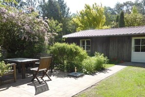 A wooden building with a tiled roof, a patio with a table and chairs, and a garden with various plants and a small sculpture. - Holiday home in Mölln with swimming pool (Mölln)